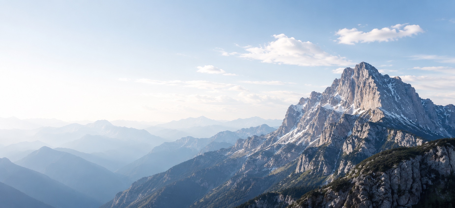 Sunlit mountain peaks rising above layers of misty ridges